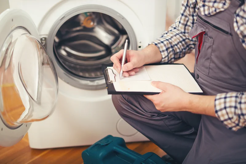 Appliance repair technician inspecting a front load washing machine with a clipboard Appliance repair technician inspecting a front load washing machine with a clipboard