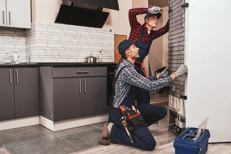 Two appliance technicians repairing the back of a refrigerator