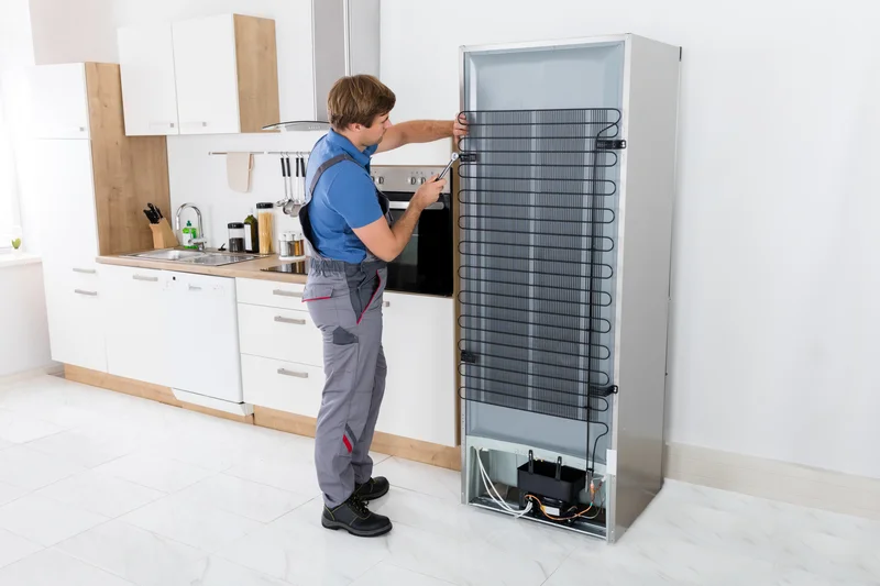 Appliance technician repairing refrigerator condenser coils in kitchen Appliance technician repairing refrigerator condenser coils in kitchen