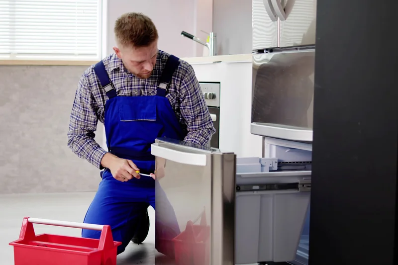 Professional technician repairing a stainless steel French door refrigerator.