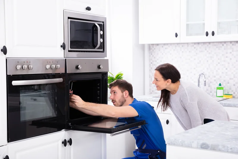 Repairman fixing a wall oven in kitchen with happy homeowner